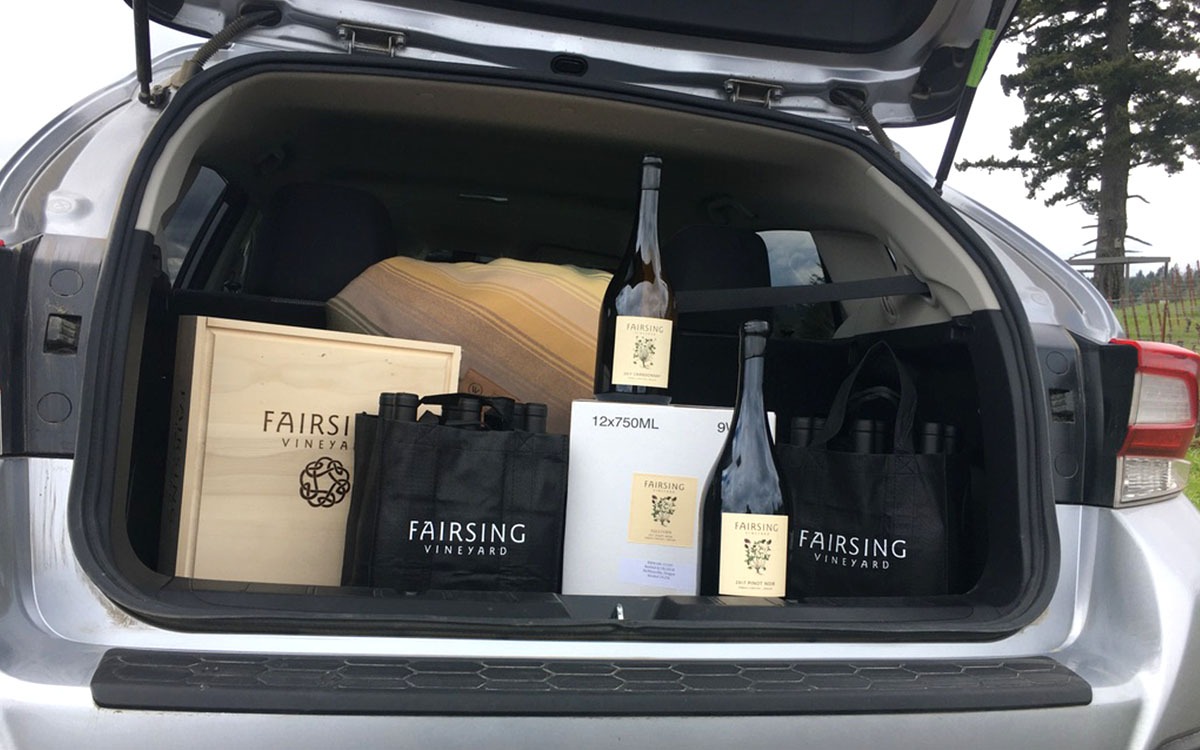 Fairsing Vineyard wines, magnums, and gifts are loaded into the back of a vehicle near a tall fir tree in the vineyard
