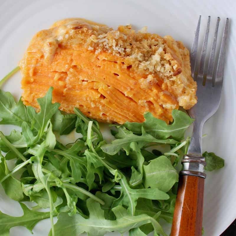 Chipotle Gratin sweet potatoes with green salad and fork on a white plate