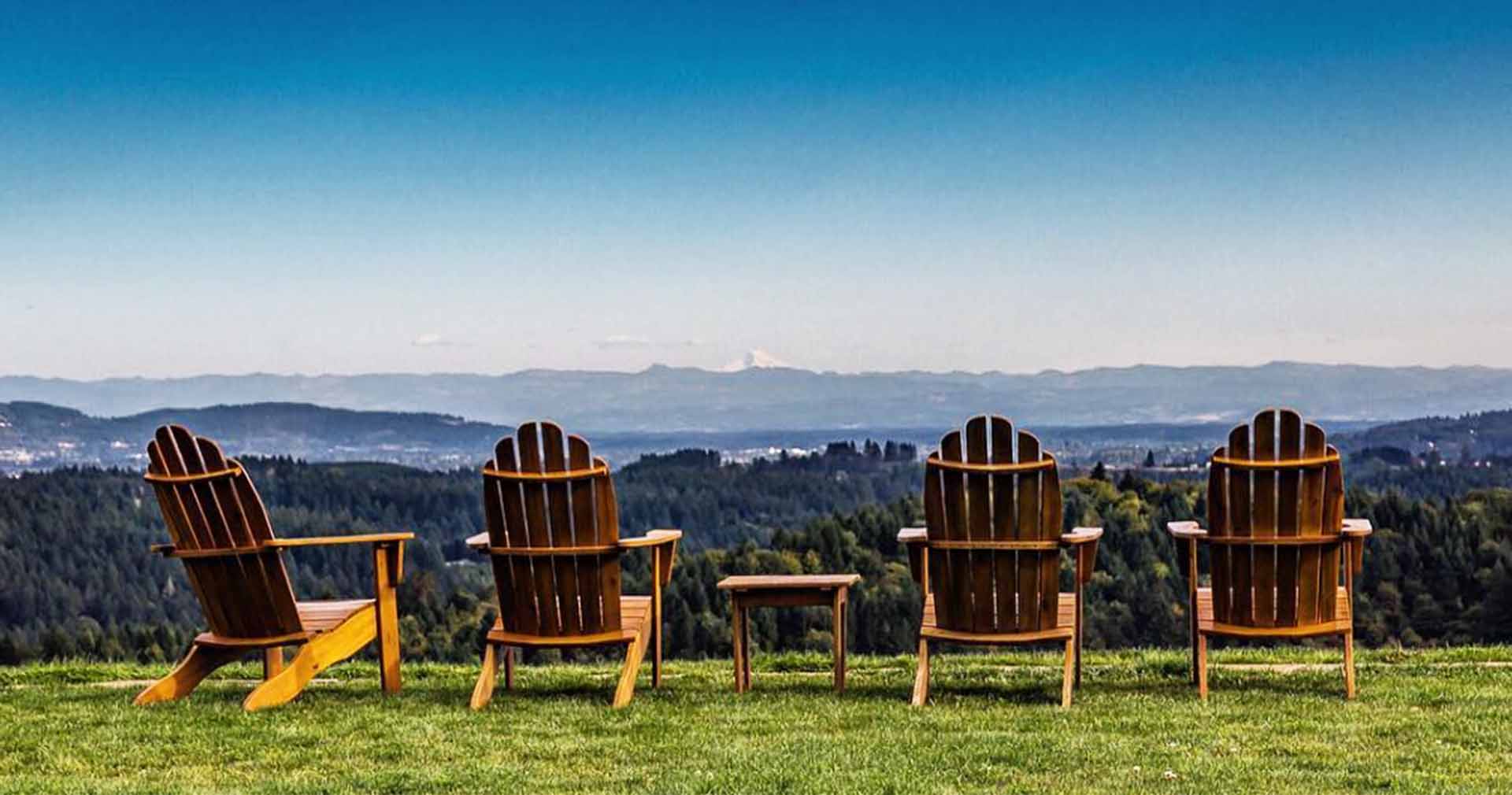 Four Adirondack chairs sit on green grass with a view of the High Cascades at Fairsing Vineyard in Oregon's Willamette Valley