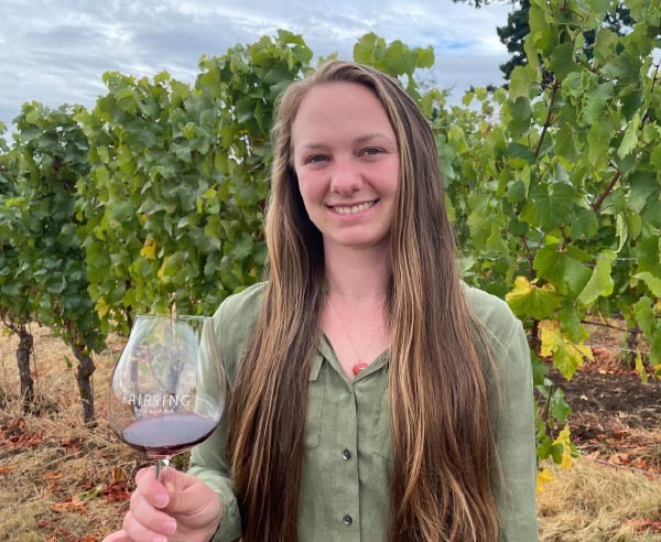 Fairsing Vineyard Tasting Room Associate Kelsey Taylor with wine glass among the vines in Oregon's Willamette Valley