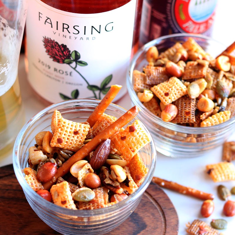 Sweet, salty, and spicy snack mix in small glass bowls with bottle of Fairsing Vineyard Rosé of Pinot noir