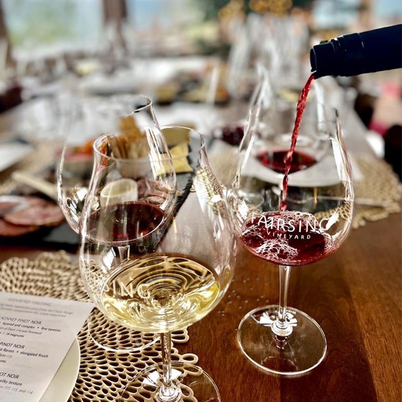 Fairsing Vineyard wine glasses and a bottle pouring the estate Pinot noir into a glass surrounded by culinary selections