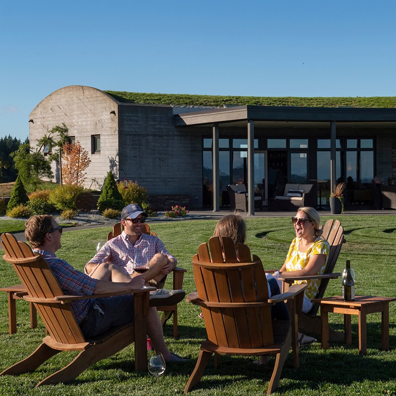 Four individuals in lawn chairs enjoy wine on the green lawn outside of Fairsing Vineyard in Oregon's Willamette Valley