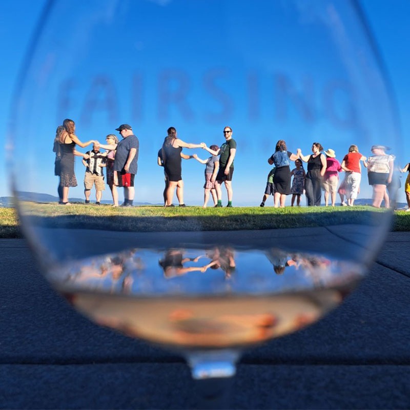 Guests participate in a Ceili Irish dance at Fairsing Vineyard as seen through a wine glass with a splash of Rosé of Pinot noir